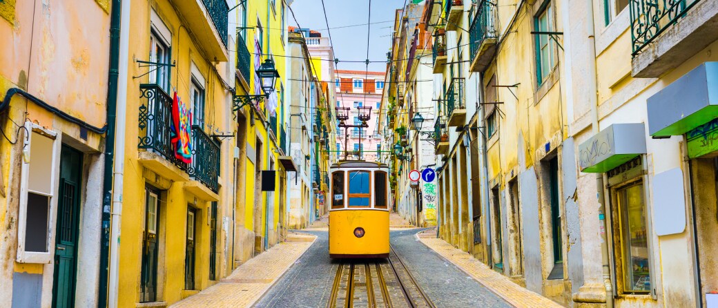 Ground view of a colorful street on a hill in Lisbon, Portugal, with a street car heading down the hill and facing the camera.