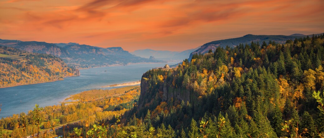 Aerial view of the Columbia River Gorge in the Fall. On the near side of the gorge is a bluff filled with trees with orange colored leaves.