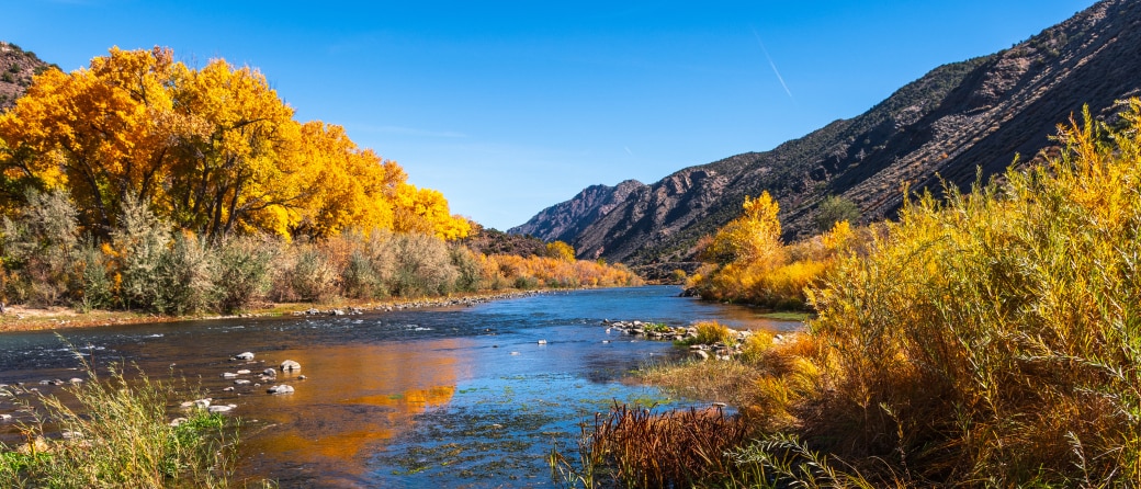 A river near Taos, New Mexico runs through a hillside filled with trees with orange colored leaves in the Fall.