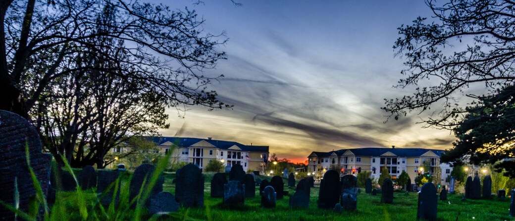 Ground view with old headstones in the foreground and a spooky looking sky overhead in Salem, Massachusetts.