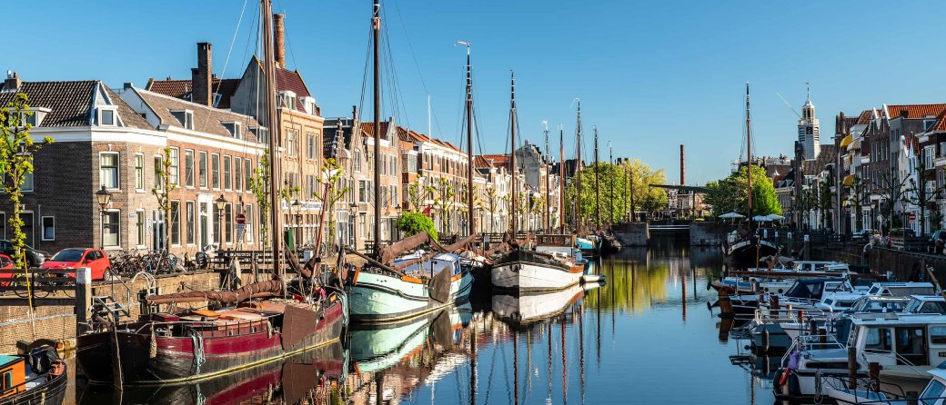 View from a bridge of a canal in Rotterdam, Netherlands. Moored boats line both sides of the canal. Buildings and homes line both sides of the street.