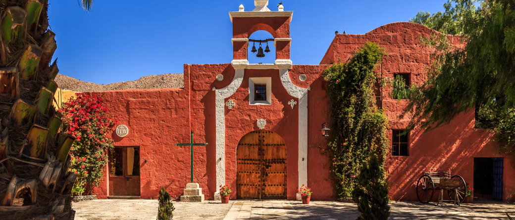 Exterior view of the Founder's Mansion in Arequipa, Peru during the day. A historic structure with orange stucco and three bells above the main entry.