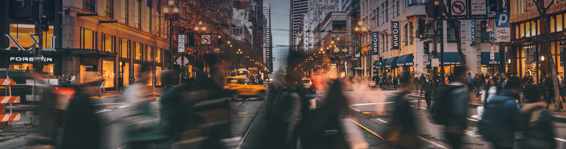 Ground view of a busy New York City, with people walking both directions through a crosswalk.