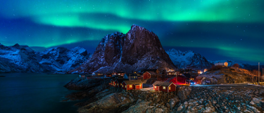 A small village by the sea at night with the northern lights displayed overhead.