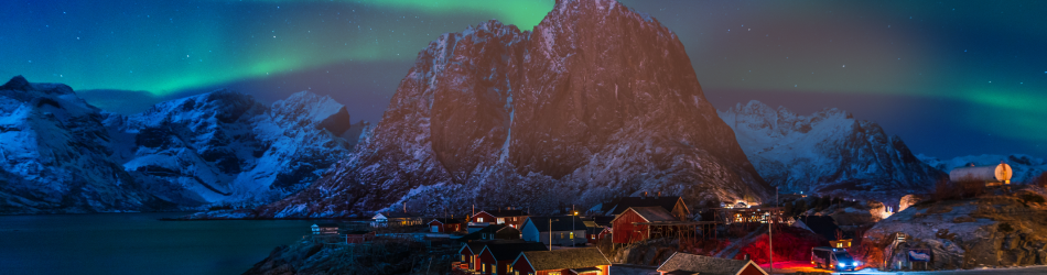 A small village by the sea at night with the northern lights displayed overhead.