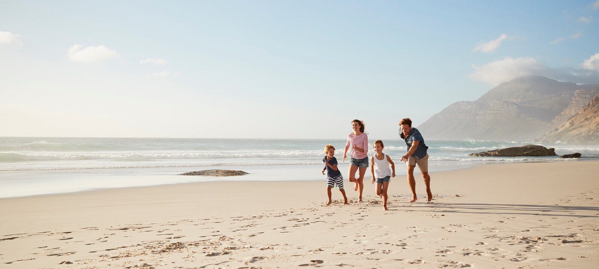 A young family of four is running together at the beach on a warm summer evening.