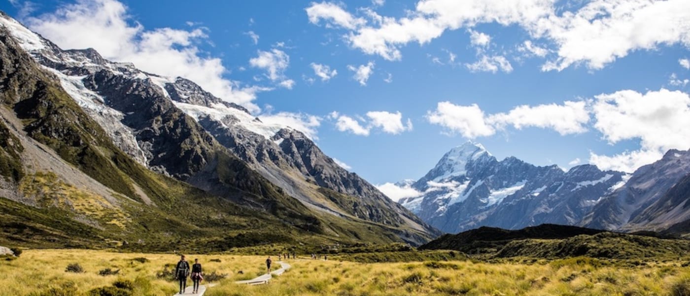 People walking along a raised path into a vast valley in scenic New Zealand.