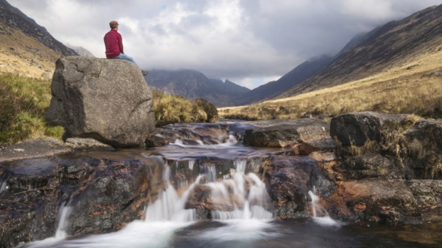 person standing next to small waterfall in the scottish countryside