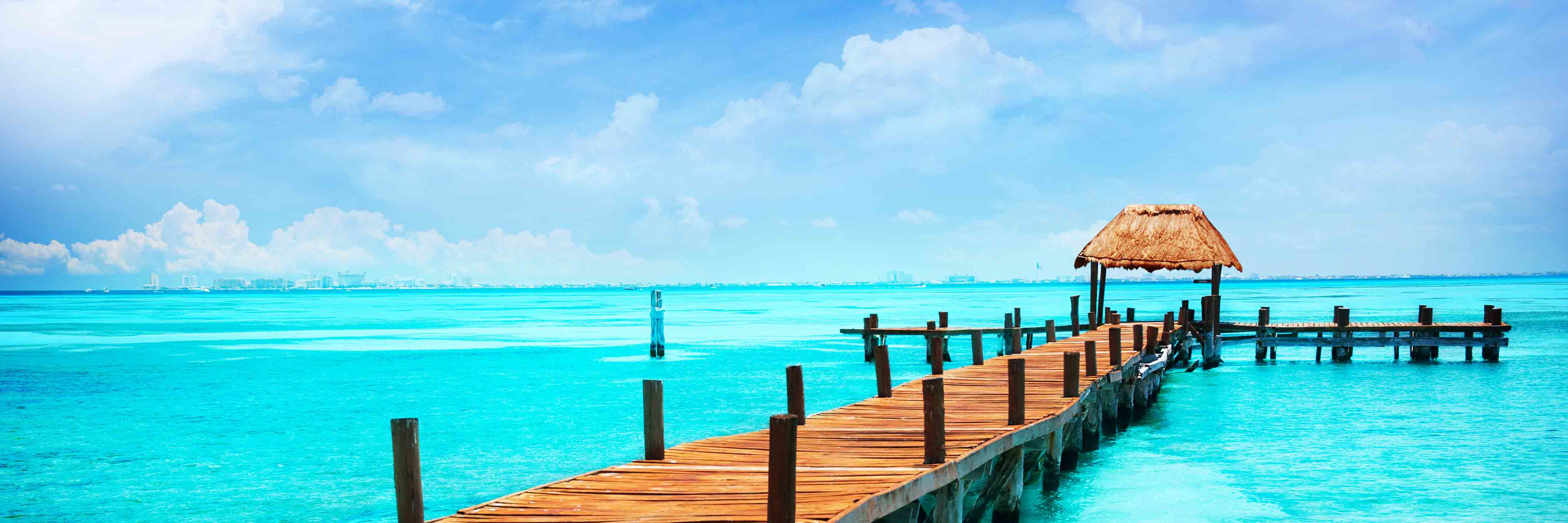 A brown beach hut in Mexico jutting out into a beautiful blue calm sea.
