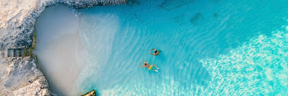 A couple swims toward a secluded beach opening.