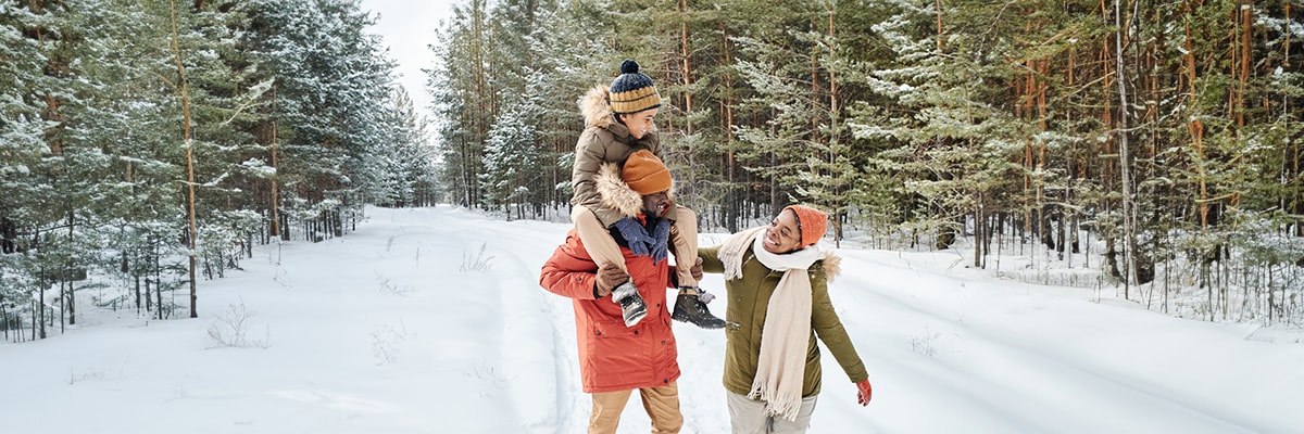 Un couple et leur enfant se balladent dans les bois enneiges.