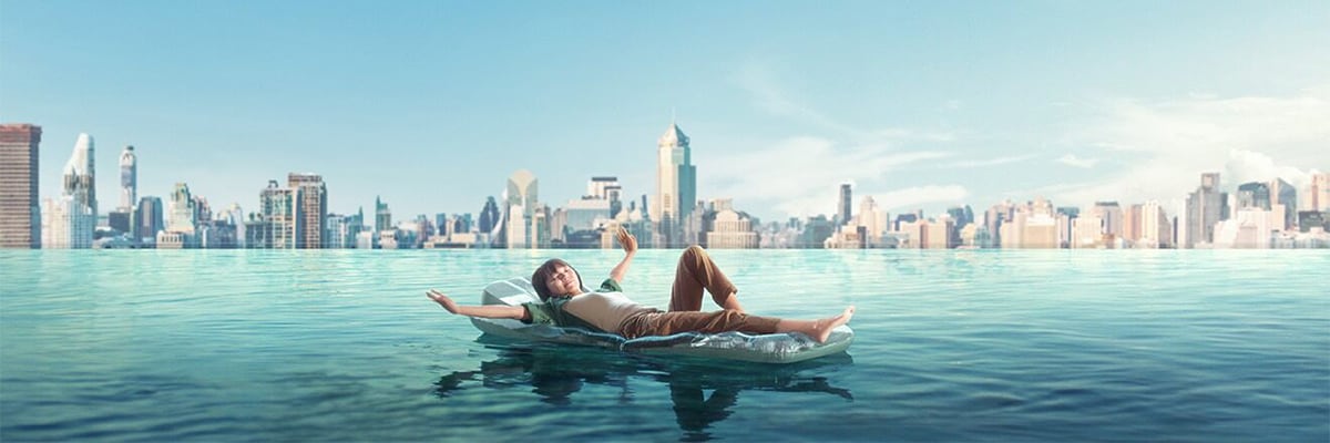 Female laying on a pool float in an infinity pool over looking the city scape.
