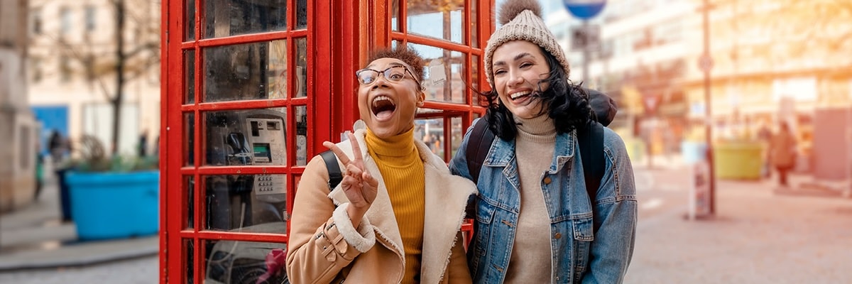 Two friends stand in front of a red telephone booth in London.