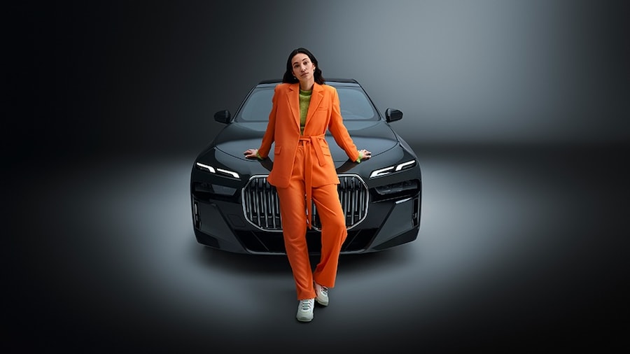 A woman in an orange dress leans up against a black convertible rental car. Sixt Car Rentals.