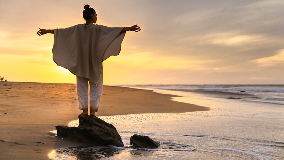 A woman's outstretched arms embrace a beach sunset.