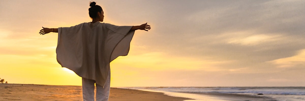 A woman's outstretched arms embrace a beach sunset.