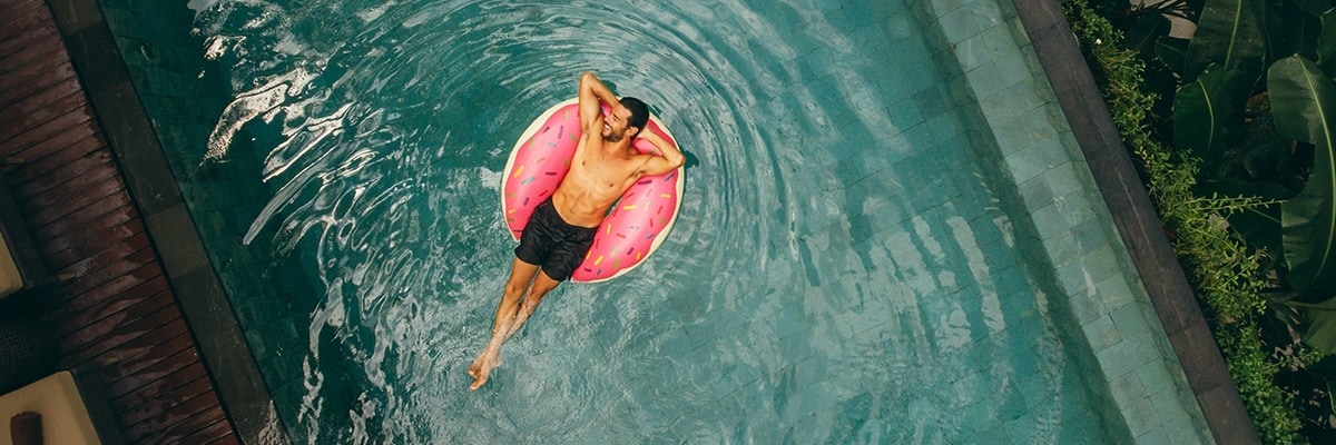 A man floats in a pool on a donut style raft.