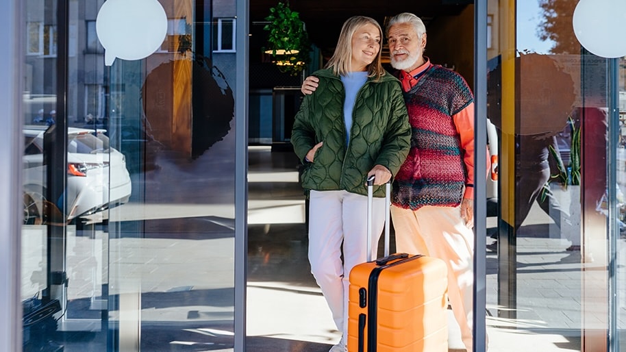 A couple at a hotel with an orange roller suitcase.