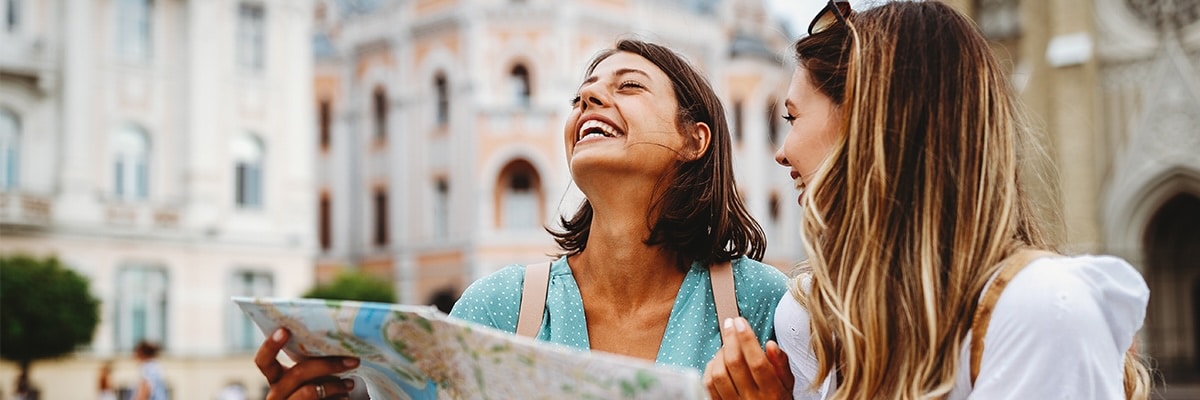 Two women laugh and look at a map as they explore the city around them.