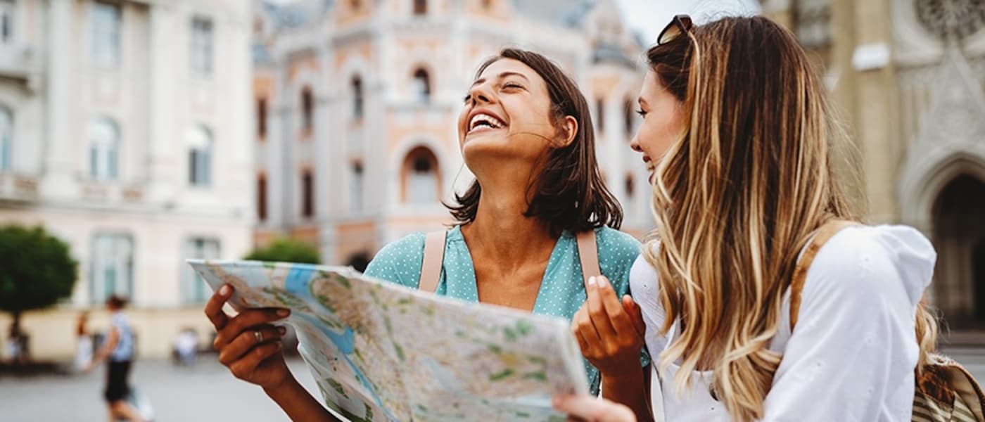 Two women laugh and look at a map as they explore the city around them.