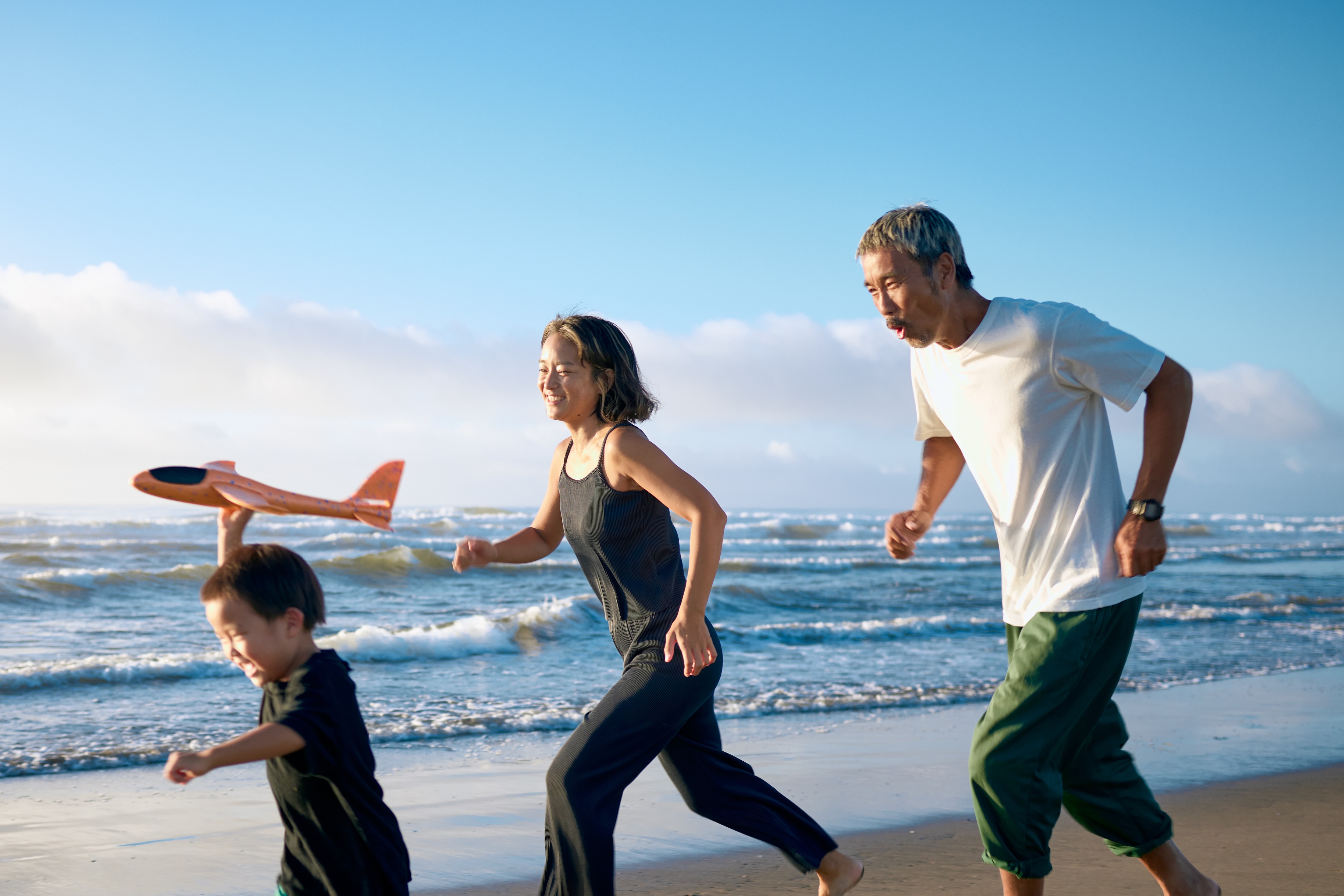 A boy and his parents running on the beach.