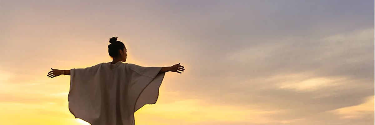 A woman&#x27;s outstretched arms embrace a beach sunset.