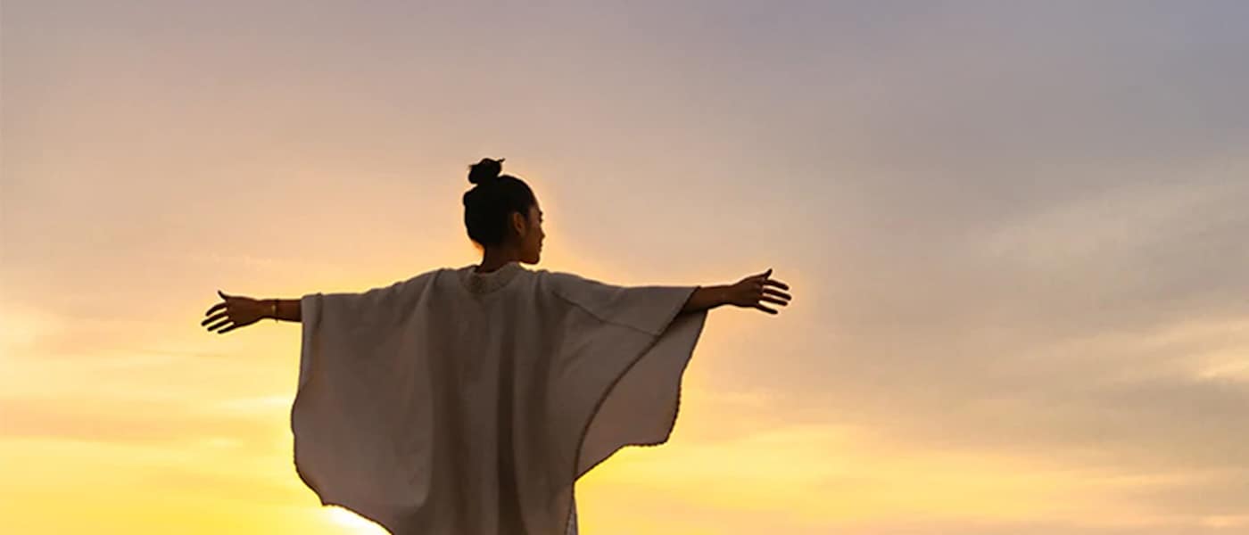 A woman's outstretched arms embrace a beach sunset.