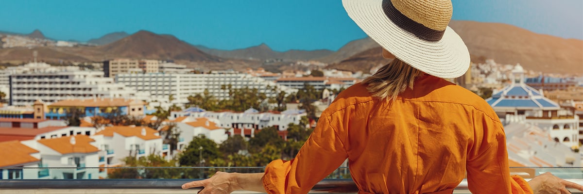 Woman standing on balcony and enjoying view to the Playa de las Americas holiday resort skyline in Tenerife