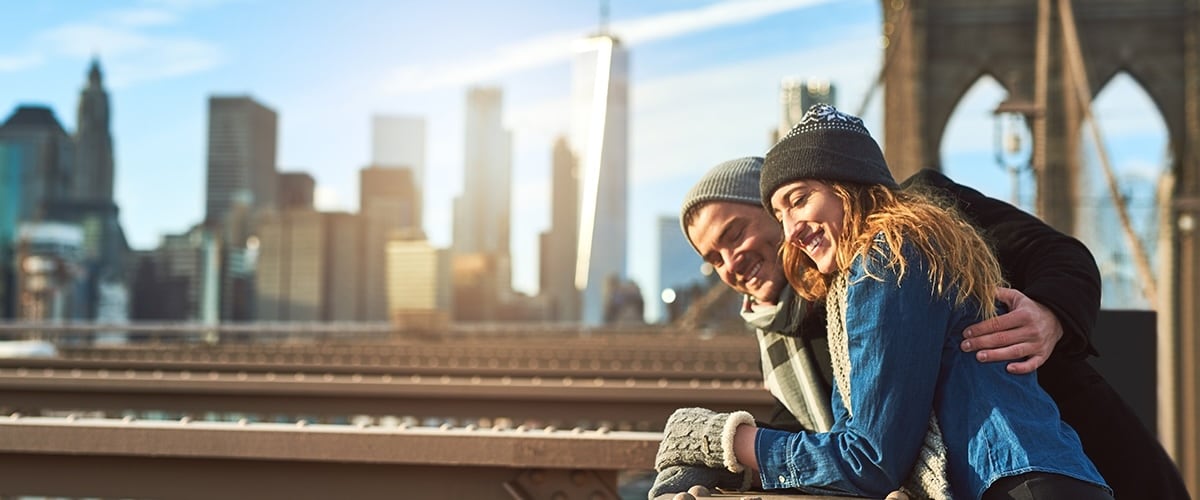 A man and woman on the Brooklyn Bridge with a view of the Manhattan skyline.