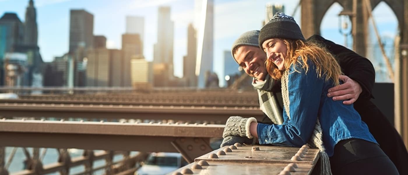 A man and woman on the Brooklyn Bridge with a view of the Manhattan skyline.
