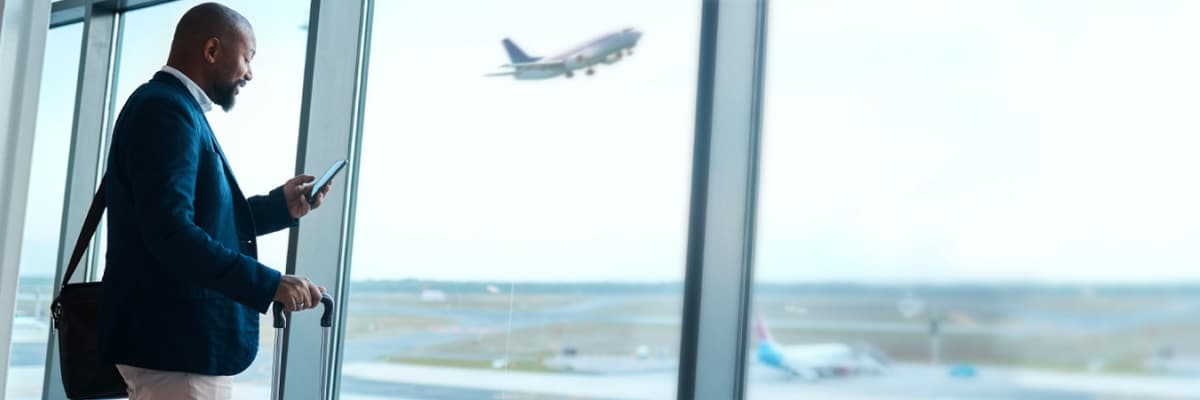 man checking phone at airport with airplane taking off in background