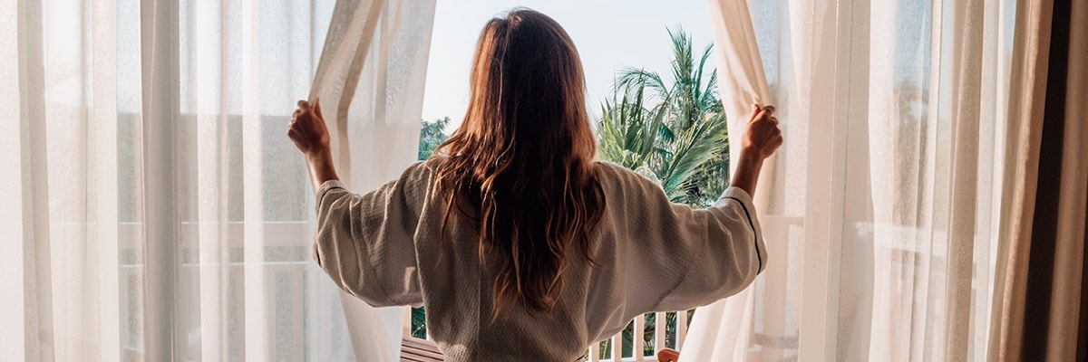 A woman looks out the window of a hotel room.