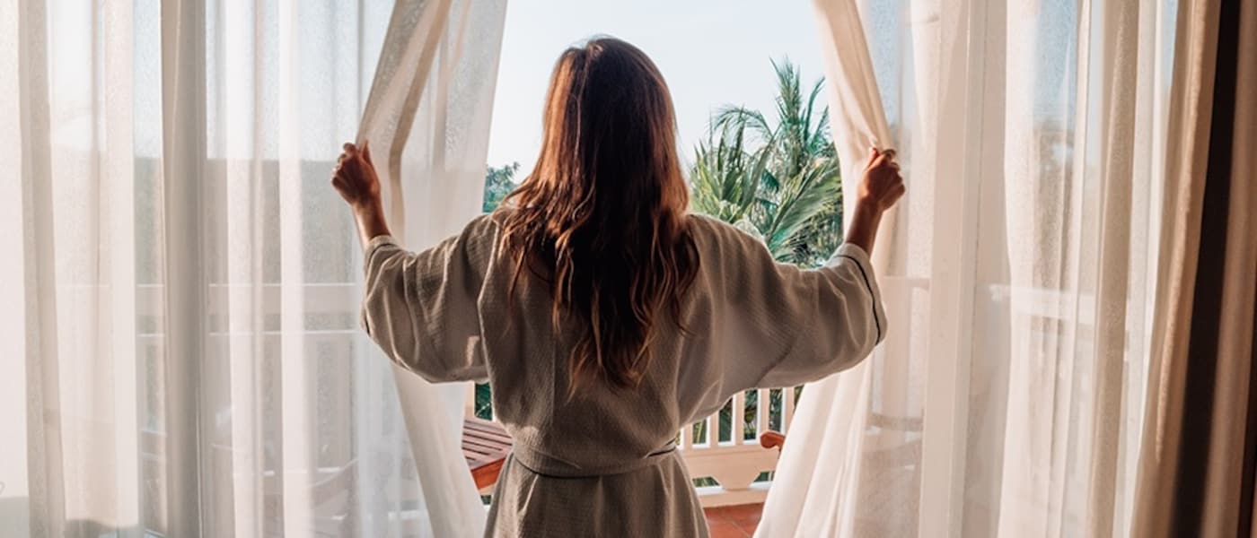 A woman looks out the window of a hotel room.