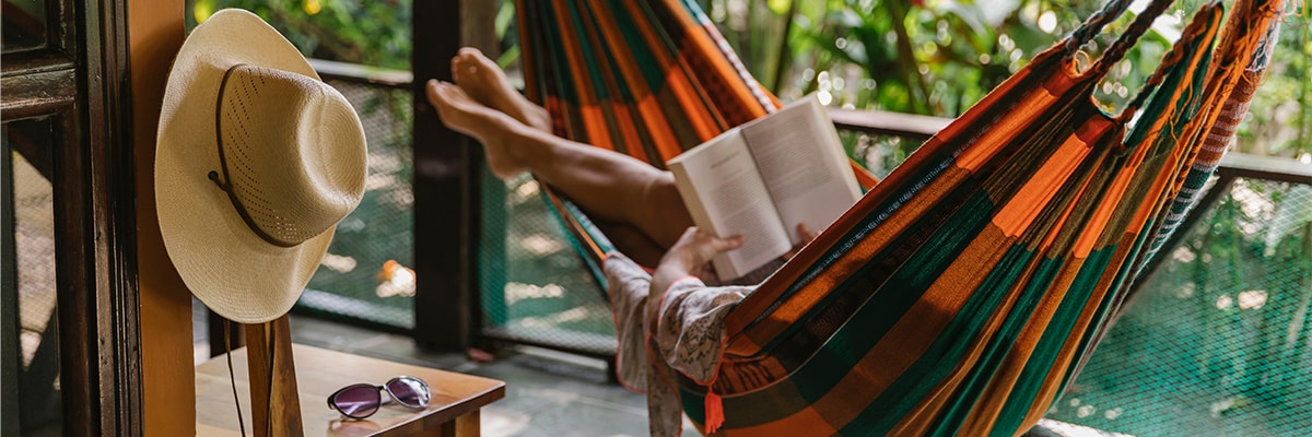 Someone lying on a hammock reading a book