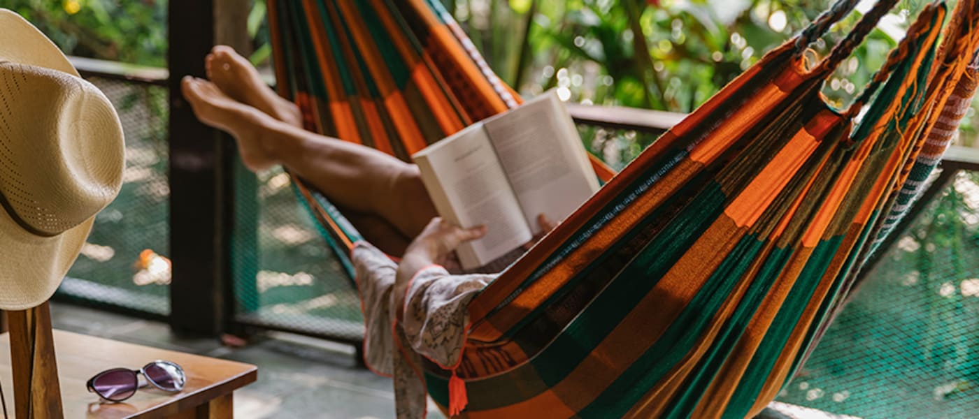 Someone lying on a hammock reading a book