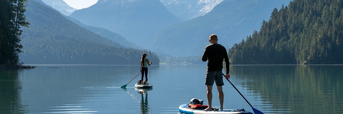 Man and woman paddle boarding in lake with mountains
