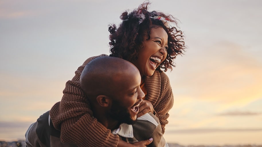 A couple laughs together as they enjoy a sunset.