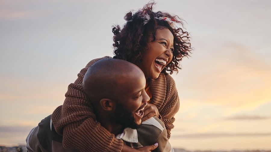 A couple laughs together as they enjoy a sunset.