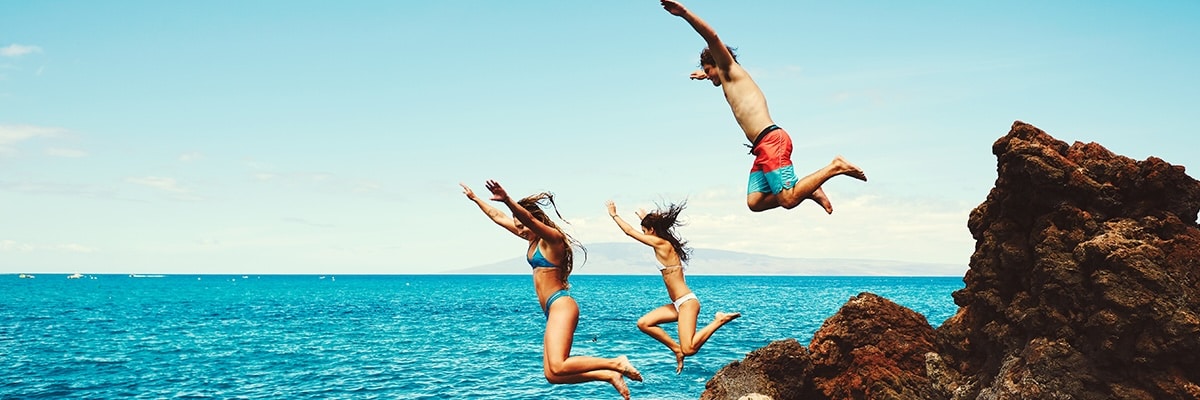 Three friends jumping from rocks into the ocean in Maui.