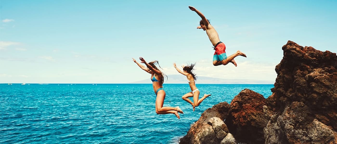 Three friends jumping from rocks into the ocean in Maui.