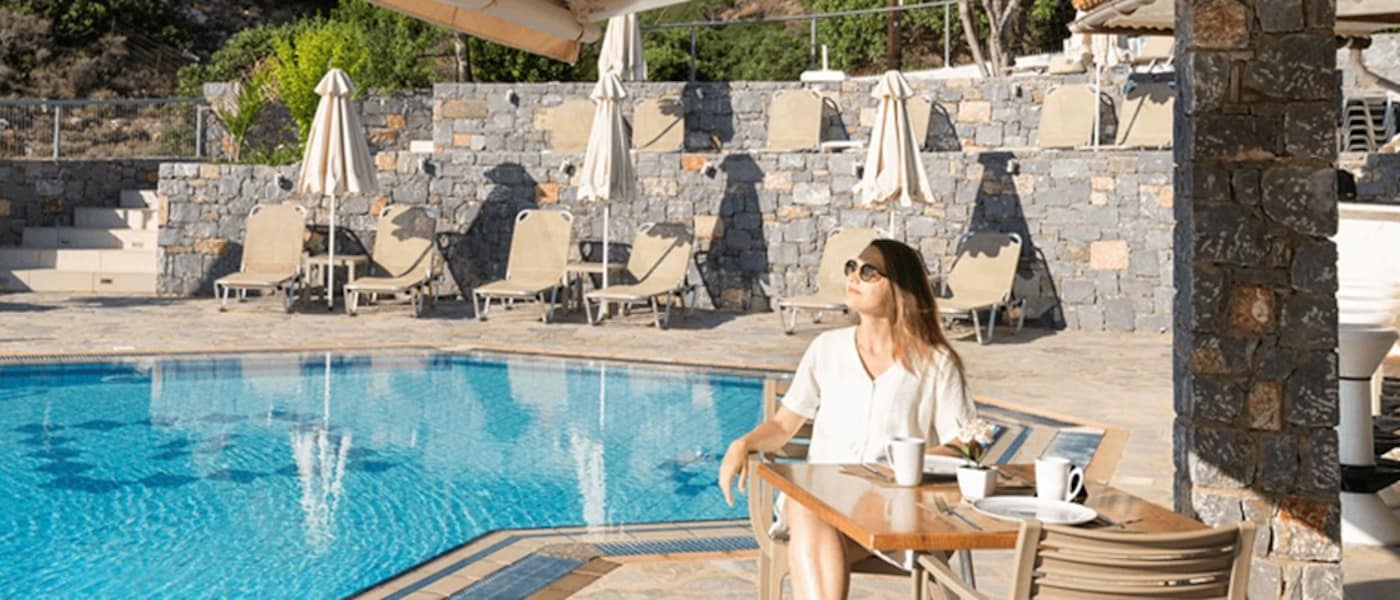 A woman in sunglasses enjoys the sun while poolside.