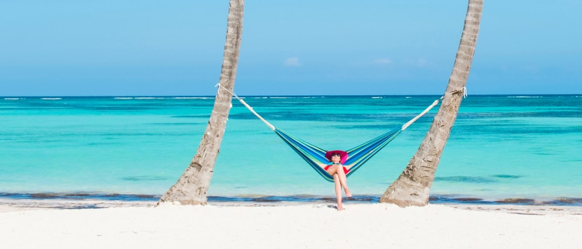 A person relaxing in a colorful hammock on a white sand beach.