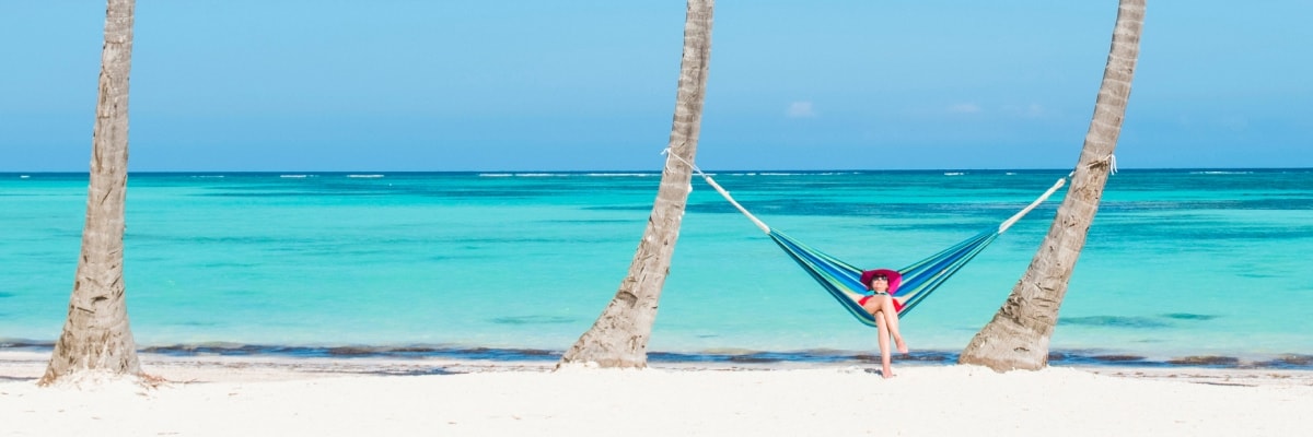 A person relaxing in a colorful hammock on a white sand beach.