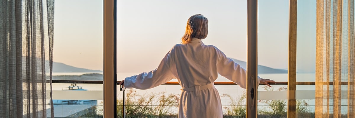 A woman looks out from a hotel balcony at sunrise.
