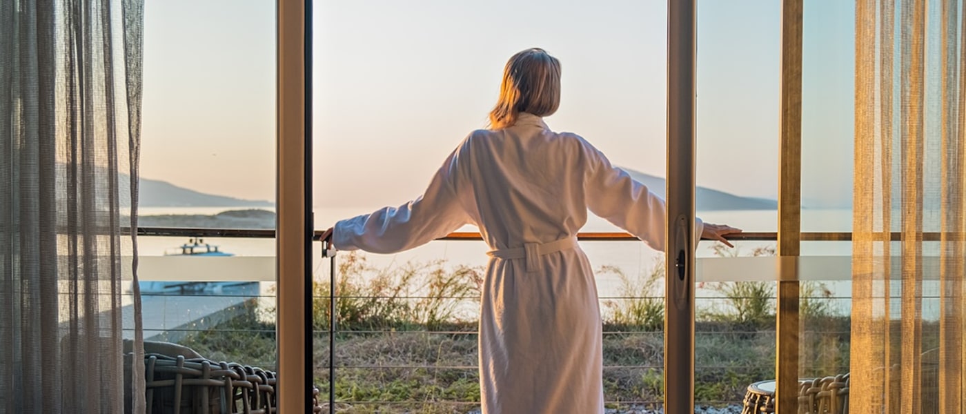 A woman looks out from a hotel balcony at sunrise.
