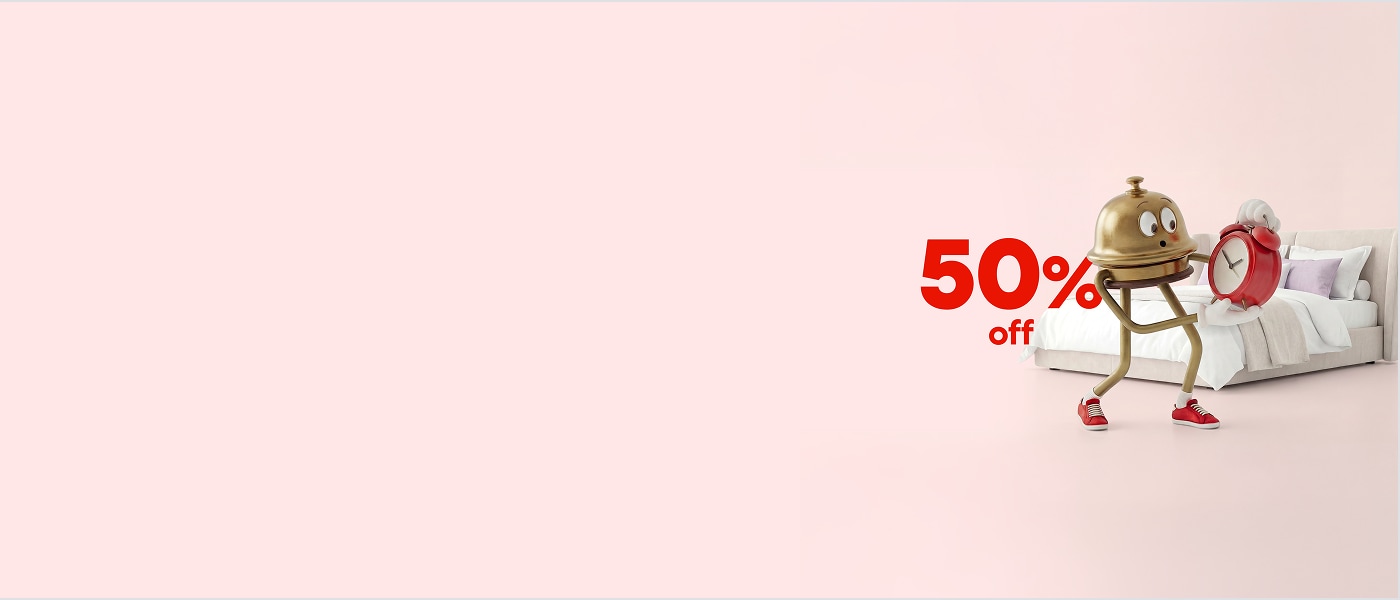 Hotels.com's mascot, Bellboy, holds a red alarm clock and stands by a bed. Bold red text reads "50% off".