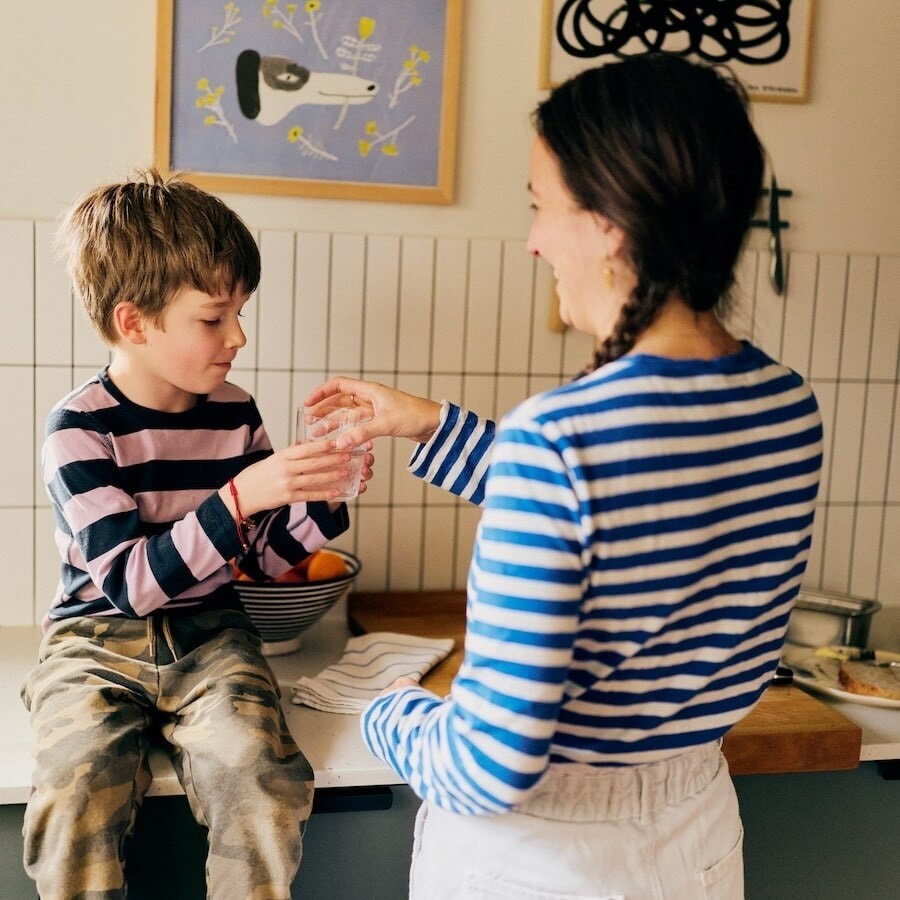 Adult and child sharing a glass of water in a cozy kitchen
